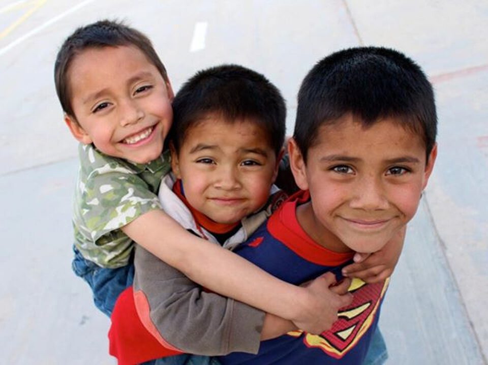 Drei Jungen spielen draußen, zwei tragen den dritten huckepack auf dem Rücken.