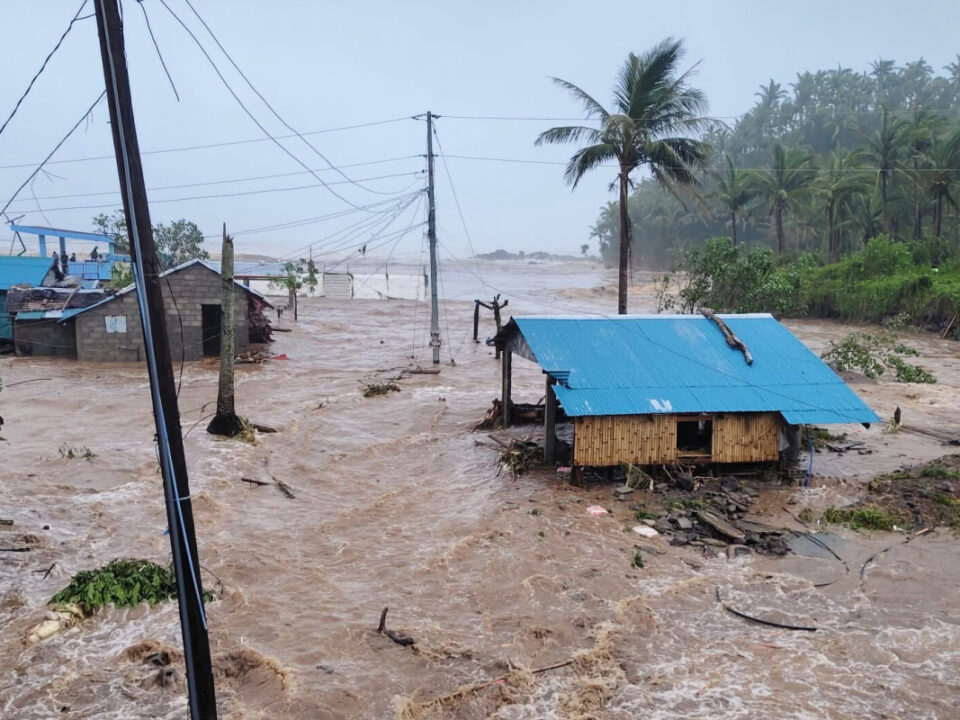 Überschwemmte Häuser und Straßen nach einem Taifun auf den Philippinen, braunes Hochwasser fließt durch die Siedlung.